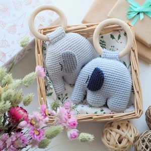 Puede incluir: Dos sonajeros de beb&eacute; de elefante de crochet con anillos de madera en una cesta de mimbre. Los elefantes son de color azul claro y gris con detalles bordados. La cesta est&aacute; forrada con una tela blanca con un patr&oacute;n floral.