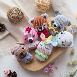 Puede incluir: Una colección de seis animales de peluche tejidos a crochet, incluyendo un unicornio, un flamenco, un gato, un perro, un oso y un lobo. Todos los animales llevan lazos y están sentados en una tabla de cortar de madera.