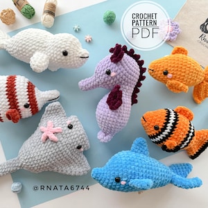 Könnte beinhalten: Eine Sammlung handgefertigter Häkeltiere aus dem Meer, darunter ein weißer Delfin, ein rot-weiß gestreifter Fisch, ein grauer Rochen, ein lila Seepferdchen, ein oranger Fisch, ein orange-schwarzer Clownfisch und ein blauer Delfin. Der Text "CROCHET PATTERN PDF" ist enthalten.