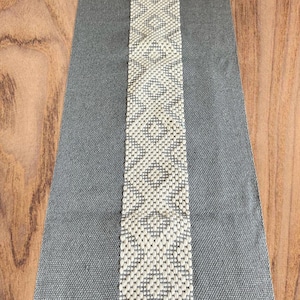 Peut inclure: Un chemin de table gris avec un motif géométrique blanc au centre.