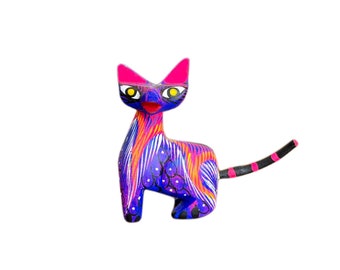 Könnte beinhalten: Eine handbemalte Holzkatzenfigur mit einem violetten, blauen und orangenen Design. Die Katze hat rosa Ohren und einen schwarzen Schwanz mit weißen Streifen.
