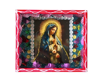 Può includere: Un'immagine incorniciata della Vergine Maria con un abito blu e una corona d'oro, che tiene un mazzo di rose. La cornice è decorata con paillettes, glitter e fiori di carta in tonalità rosa, blu e verde.