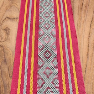 Peut inclure: Un chemin de table rayé rouge, jaune et gris avec un motif géométrique au centre.