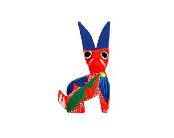 May include: A red, blue, and green painted wooden rabbit figurine. The rabbit has a blue head and ears, a red body, and green and blue floral designs.