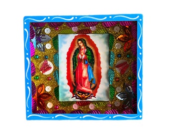 May include: A blue wooden frame with a gold glitter background and a colorful image of the Virgin Mary inside. The frame is decorated with sequins and other embellishments.
