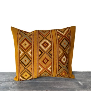 May include: A mustard yellow throw pillow with a geometric pattern in shades of brown, red, and gray. The pillow is made of a soft, woven fabric and has a subtle sheen.