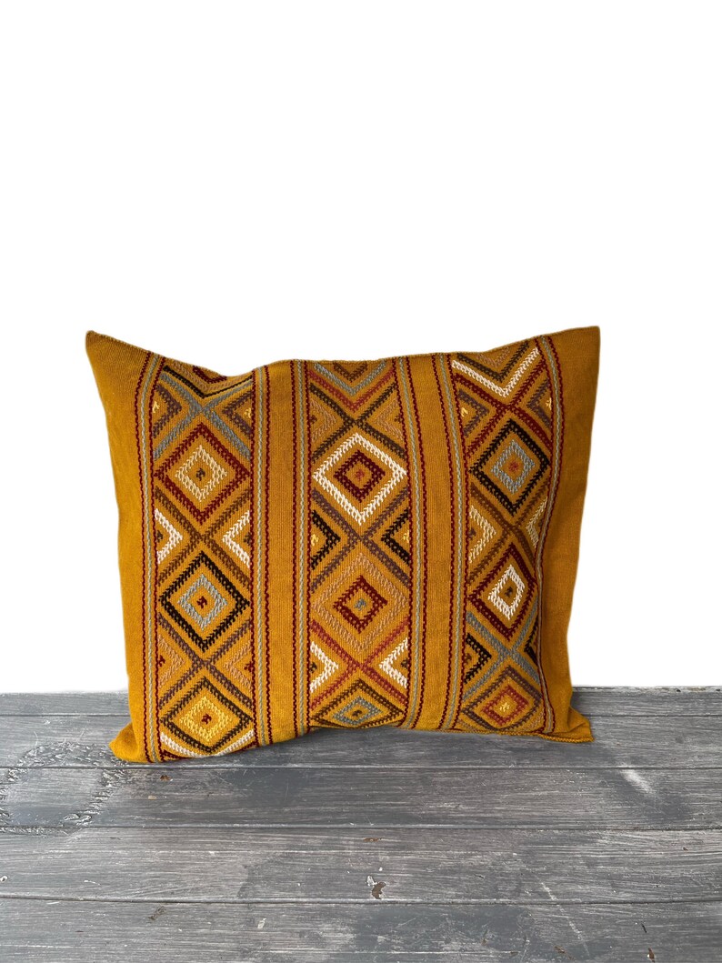 May include: A mustard yellow throw pillow with a geometric pattern in shades of brown, red, and gray. The pillow is made of a soft, woven fabric and has a subtle sheen.