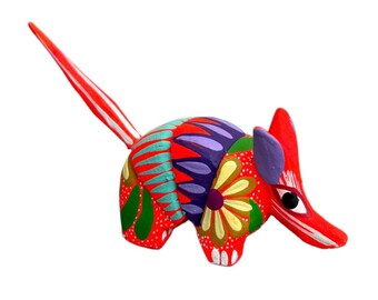 May include: A vibrantly painted wooden armadillo figurine. The folk art piece features a red body with floral and dot patterns in green, yellow, purple, and turquoise. The tail is red and white striped.