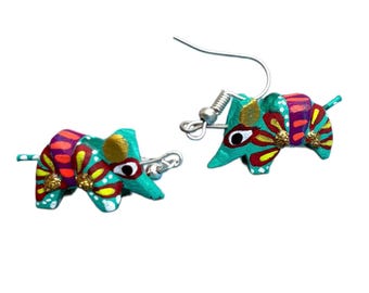 May include: A pair of handcrafted, colorful armadillo earrings. Each earring features a teal body with red, yellow, and purple floral patterns. The armadillos have black eyes and gold glitter accents. The earrings are suspended from silver-tone ear wires.