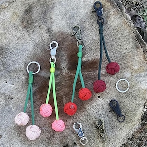 May include: Five keychains with different colored cords and metal clasps. Each keychain has a knotted ball at the end of the cord. The balls are red, green, and pink.