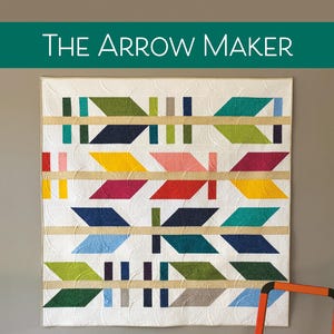 May include: A colorful quilt titled "The Arrow Maker" with a repeating arrow pattern in various colors. The quilt is displayed on a wall with an orange step ladder. The text "Use a Dessert Roll of 5" strips or Fat Quarters" is visible.