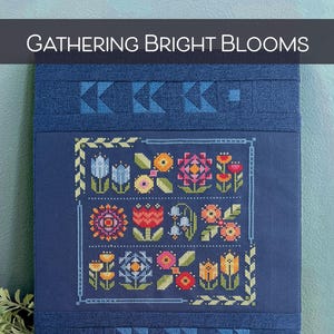 Könnte beinhalten: Ein Kreuzstichmuster mit dem Titel "Gathering Bright Blooms" von Robin Pickens. Das Muster zeigt eine Vielzahl von bunten Blumen und Blättern auf einem dunkelblauen Hintergrund.