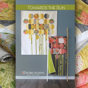 Puede incluir: Un patrón de acolchado titulado "Towards the Sun" de Robin Pickens. El patrón presenta un diseño geométrico con círculos, cuadrados y rayas en tonos de amarillo, verde y gris.