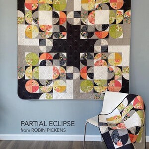 Peut inclure: Une grande courtepointe color&eacute;e avec un motif g&eacute;om&eacute;trique de demi-cercles et de carr&eacute;s dans des tons de noir, gris, blanc, orange, vert et motifs floraux. Une plus petite courtepointe avec le m&ecirc;me motif est drap&eacute;e sur une chaise blanche. Le texte sur le mur indique "PARTIAL ECLIPSE from ROBIN PICKENS."