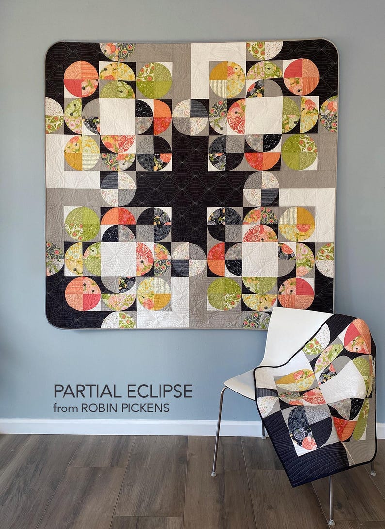 Peut inclure: Une grande courtepointe color&eacute;e avec un motif g&eacute;om&eacute;trique de demi-cercles et de carr&eacute;s dans des tons de noir, gris, blanc, orange, vert et motifs floraux. Une plus petite courtepointe avec le m&ecirc;me motif est drap&eacute;e sur une chaise blanche. Le texte sur le mur indique "PARTIAL ECLIPSE from ROBIN PICKENS."