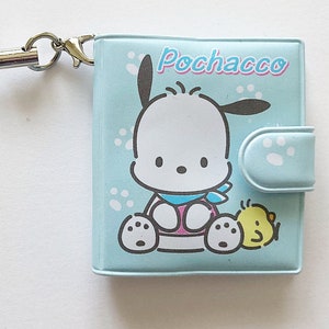 May include: A light blue wallet featuring a cartoon dog and chick design. The wallet has a flap with a snap closure and a light blue lanyard with a silver clasp.