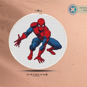 Puede incluir: Un punto de cruz de Spider-Man en un bastidor blanco. El superhéroe está representado con su clásico traje rojo y azul, en una pose agachada. El diseño está sobre un fondo neutro. El texto "Pattern Keeper Tested" es visible.