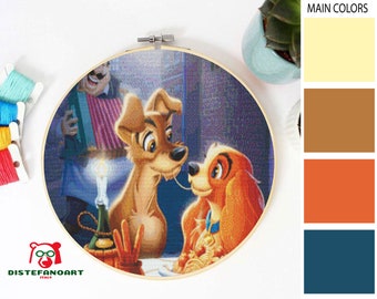 May include: A cross-stitch embroidery hoop with a scene from the Disney movie Lady and the Tramp. The image shows Lady and Tramp sharing a plate of spaghetti with a candle in the background. The colors in the image are brown, orange, yellow, and blue.