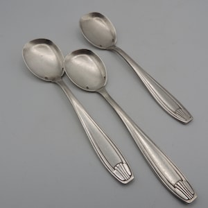 May include: Three silver spoons with ornate handles. The spoons have a rounded bowl and a slightly curved handle.