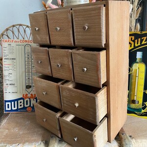 May include: A wooden spice rack with ten small drawers, each with a silver knob. The rack is made of light-colored wood and has a rustic, vintage appearance. The drawers are open, suggesting they are ready to be filled.