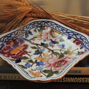 Peut inclure: Un plat de service en céramique blanche avec un motif floral bleu et blanc. Le plat a un bord festonné et est décoré de fleurs et de feuilles colorées.