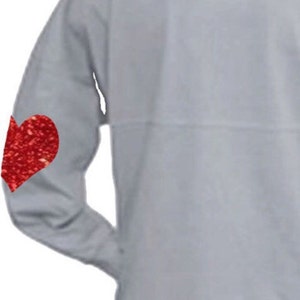 Op de afbeelding: Een grijs longsleeve shirt met een rood glitterhart op de linkermouw.
