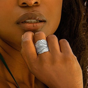 May include: A woman with long, dark hair is wearing a green halter top and a silver ring with a leaf design.