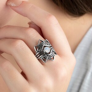 Könnte beinhalten: Ein silberner Ring mit einem weißen Mondstein in der Mitte und filigranen floralen Designs. Der Ring wird an einem Finger getragen.