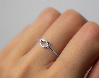 Op de afbeelding: Een zilveren knoop ring op een hand.