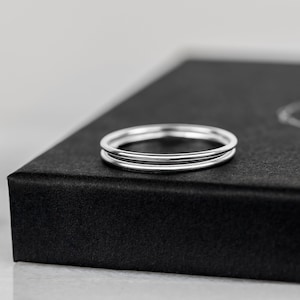 May include: Two thin silver rings stacked on top of each other, displayed on a black box.