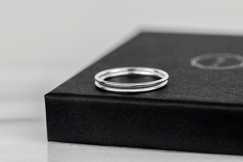 May include: Two thin silver rings stacked on top of each other, displayed on a black box.