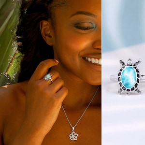 Puede incluir: Un anillo de plata con una piedra turquesa engastada en un diseño de tortuga. El anillo se lleva en el dedo de una mujer. También lleva un collar de plata con un colgante de flor.