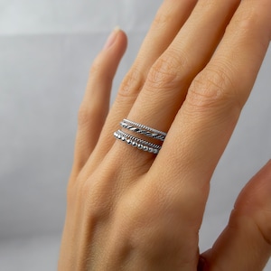 May include: A set of three silver rings stacked on a finger. The top ring is a thin band, the middle ring is a twisted band, and the bottom ring is a band with small beads.