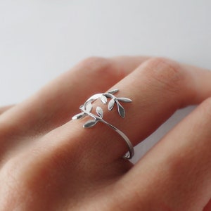 Puede incluir: Un anillo de plata con un delicado diseño de hojas. El anillo es abierto y ajustable para adaptarse a diferentes tamaños de dedos.