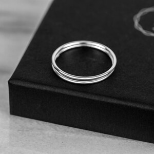 May include: A silver ring with three bands, stacked on top of each other. The ring is on a black surface.