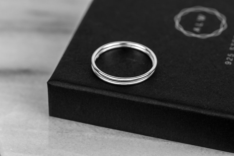 May include: A silver ring with three bands, stacked on top of each other. The ring is on a black surface.