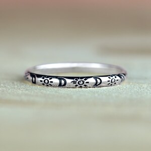 Peut inclure: Une bague en argent avec un motif soleil et lune. La bague est gravée d'un motif répétitif de soleils et de lunes.