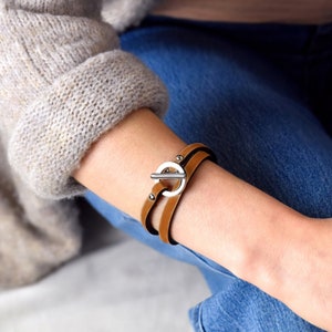 Peut inclure: Un bracelet en cuir marron avec une fermeture à boucle argentée. Le bracelet est enroulé autour du poignet d'une personne.