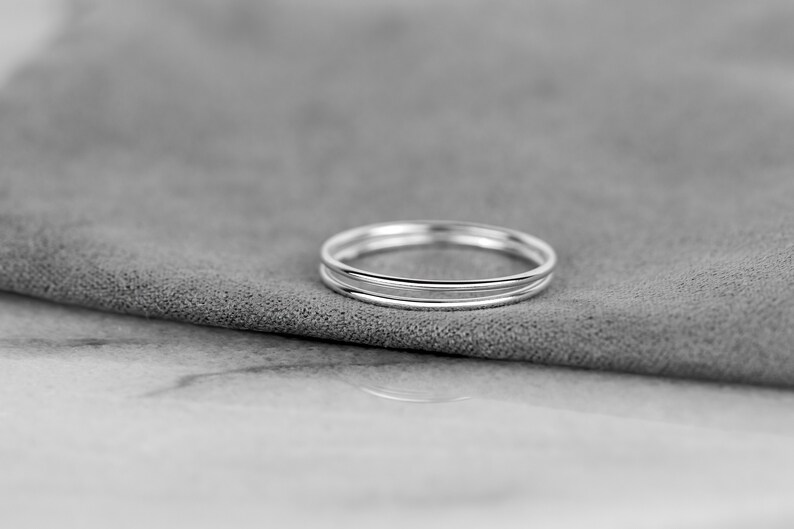 May include: A set of three thin silver rings stacked on top of each other. The rings are smooth and shiny.
