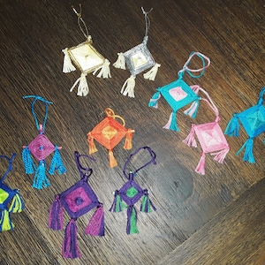 May include: A collection of ten colourful dreamcatchers with fringe, each with a different colour scheme. The dreamcatchers are handmade and feature a variety of colours, including blue, green, purple, pink, orange, and gold.