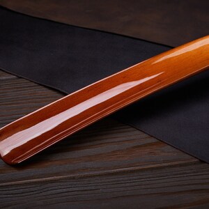 May include: A wooden shoehorn with a glossy, reddish-brown finish. The shoehorn is lying on a dark wooden surface.