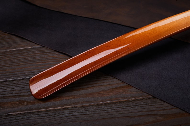 May include: A wooden shoehorn with a glossy, reddish-brown finish. The shoehorn is lying on a dark wooden surface.