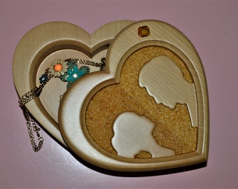 May include: A wooden heart-shaped box with a hinged lid. The box is open, revealing a smaller heart-shaped compartment inside. The smaller compartment is filled with a golden sand-like material. The larger compartment contains a gold chain necklace with colorful flower charms.