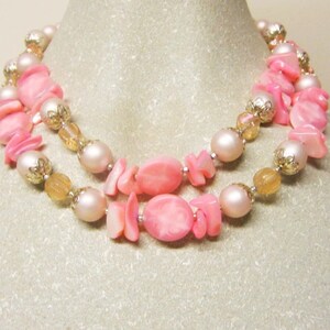 May include: A double strand necklace with pink and gold beads. The necklace features large pink shell beads and smaller gold beads with a textured surface.