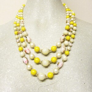 May include: A three-strand necklace with yellow and white beads. The necklace is made of glass beads and has a vintage look.