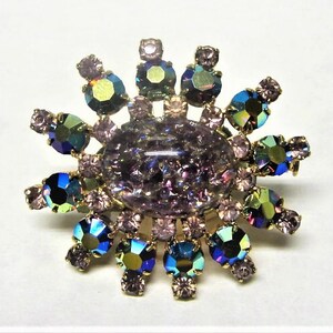 Peut inclure: Une broche dor&eacute;e avec une grande pierre ovale de couleur violette iris&eacute;e entour&eacute;e de pierres plus petites, bleues, vertes et roses iris&eacute;es.
