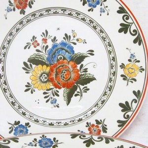 May include: Two white ceramic dinner plates with a floral design. The plates have a green and red border with a white center. The center of the plate features a bouquet of yellow, red, and blue flowers with green leaves.