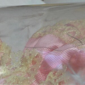 Puede incluir: Un vestido de mu&ntilde;eca de encaje rosa y amarillo con un delicado patr&oacute;n floral. El vestido est&aacute; hecho de una tela suave y fluida y tiene un estilo rom&aacute;ntico y vintage.