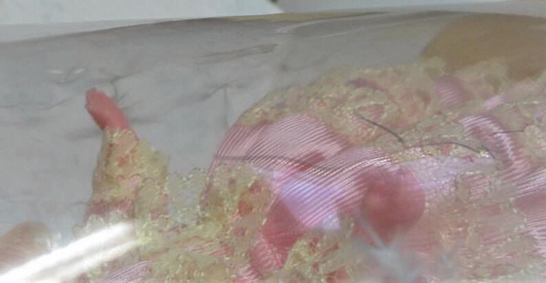Puede incluir: Un vestido de mu&ntilde;eca de encaje rosa y amarillo con un delicado patr&oacute;n floral. El vestido est&aacute; hecho de una tela suave y fluida y tiene un estilo rom&aacute;ntico y vintage.
