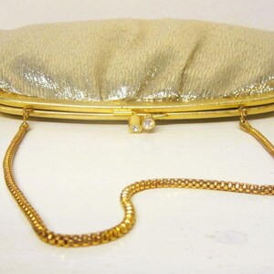 K&ouml;nnte beinhalten: Eine goldene Vintage-Clutch mit strukturierter, schimmernder Oberfl&auml;che. Die Clutch hat einen goldenen Rahmen, einen Verschluss mit zwei kleinen Strasssteinen und einen zarten goldenen Kettenriemen. Ein klassisches Accessoire f&uuml;r besondere Anl&auml;sse.